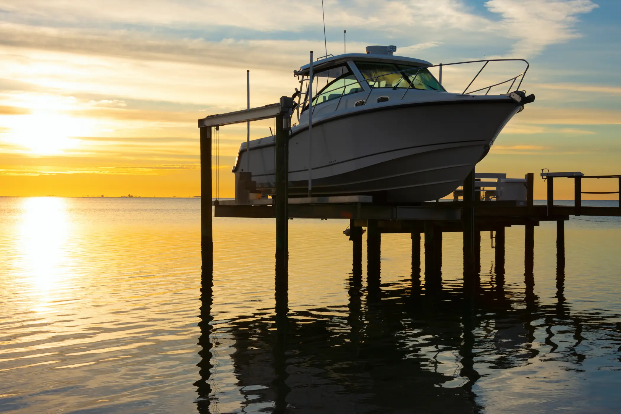 A fishing boat raised on a motorized boat lift at a waterfront dock at sunrise
