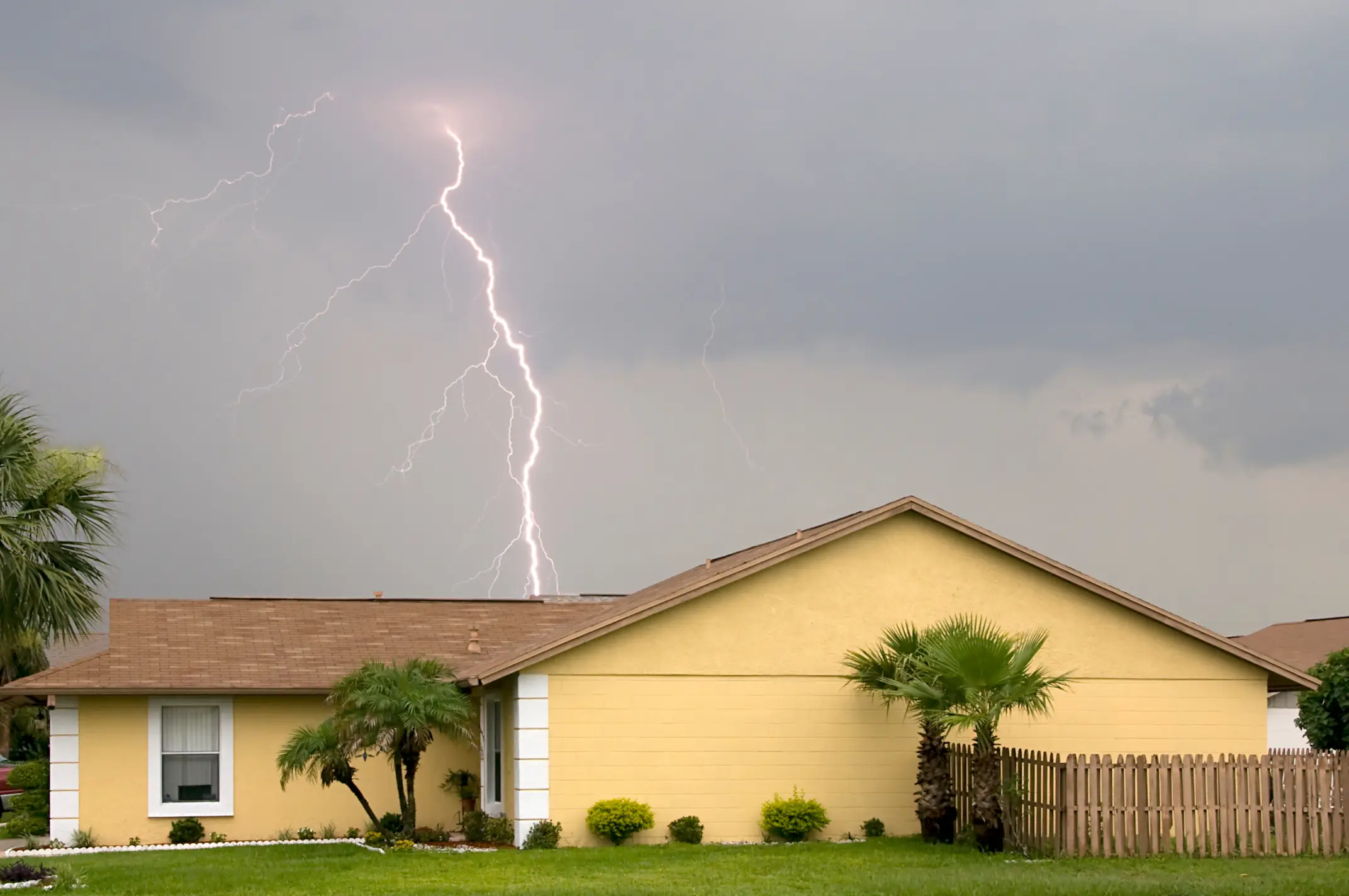 A lightning bolt striking behind a single-story Florida home with palm trees during a storm